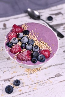 Fruit smoothie bowl with yogurt decorated with healthy raspberry, blueberry and puffed quinoa grain on iron tray