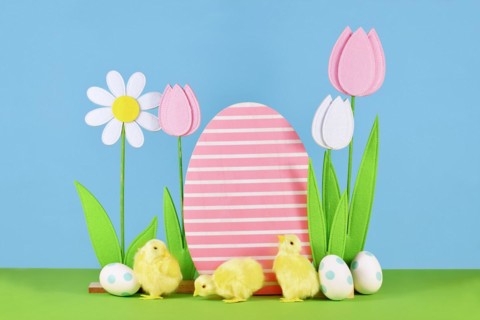 Felt spring flowers and wooden Easter egg with chicks in front of blue background
