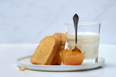 Rusk, glass of milk and orange marmalade in small bowls