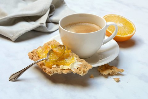 Orange marmalade in small bowls and on crispbread and cup of coffee