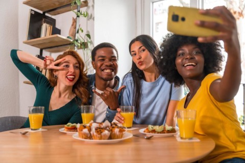 Multiethnic friends at a breakfast with orange juice and muffins at home, taking a selfie