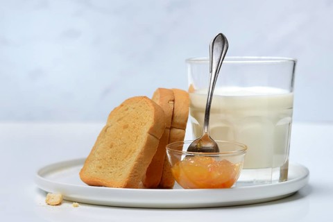 Rusk, glass of milk and orange marmalade in small bowls