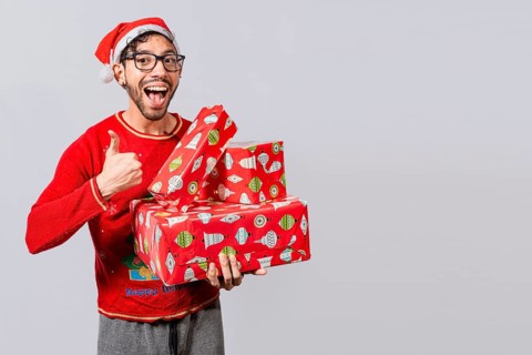 Smiling guy in christmas hat holding christmas gift boxes giving thumbs up. Friendly man in christmas clothes holding gift boxes, Christmas man holding gift boxes and smiling with thumb up