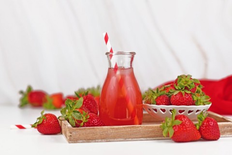 Jar with red strawberry fruit lemonade surrounded by berries