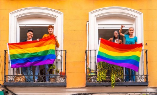 Couples of gay boys and lesbian girls with the lgtb flag on the balconies at a house party, greeting friends, LGBT pride