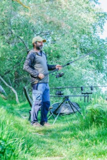 Bearded fisherman setting up his fishing gear on the river bank on a green grass field