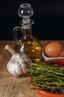 Close-up of wild asparagus in an earthenware casserole with olive oil, eggs and garlic black background