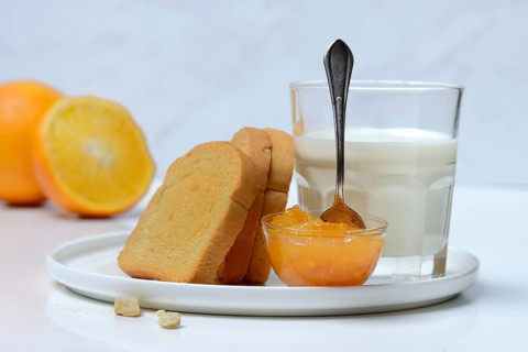 Rusk, glass of milk and orange marmalade in small bowls