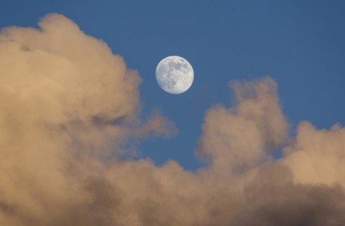 Rising full moon in the evening sky with reddish clouds