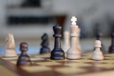Chess board game with focus on black and white queen pieces on blurry