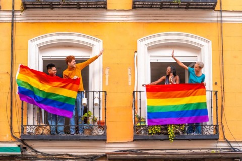 Couples of gay boys and lesbian girls with the lgtb flag on the balconies at a house party, greeting friends