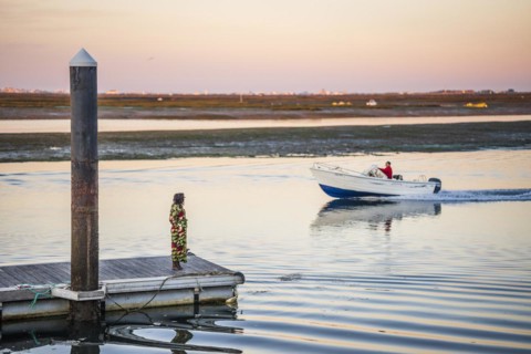 A woman on a pier looking toward a man on the boat, early morning in Faro, Algarve