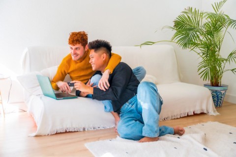 Beautiful gay couple being romantic on the sofa hugging, lgbt concept, doing online shopping