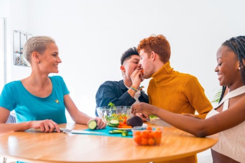 Group of friends preparing vegetarian food. Preparing the salad and having fun in the kitchen, lgtb boy couple kiss with carrot