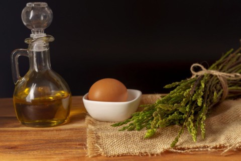Bunch of wild asparagus on a raffia cloth with a jar of olive oil and eggs black background