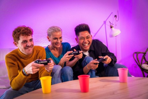 Group of young friends playing video games together on the sofa at home, purple led, having fun