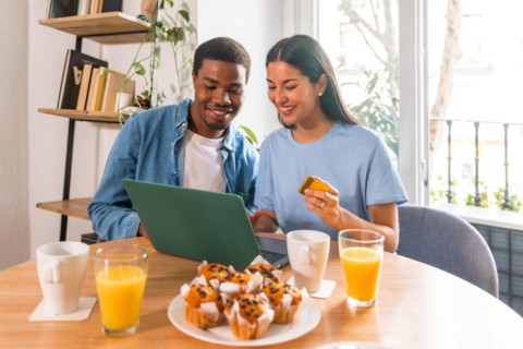 Couple making purchase online with the computer while having breakfast, next to the window, shopping on the internet