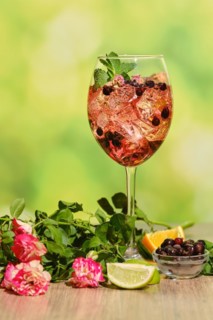 Cold sangria with dry rosebuds in wine glass with ingredients on a table over summer background