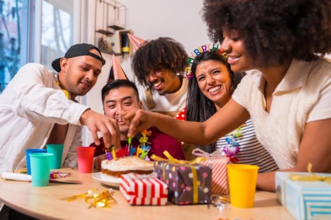 Multi-ethnic group of friends at a birthday party on the sofa at home with a cake and gifts