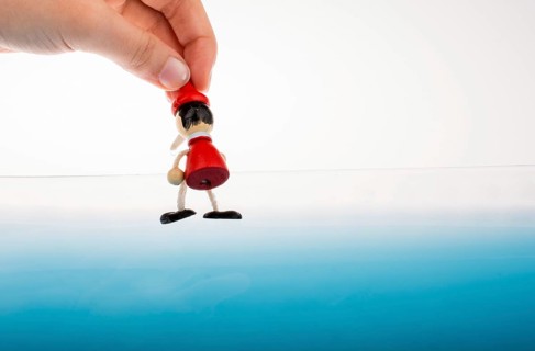 Hand holding wodden puppet Pinocchio on in blue water