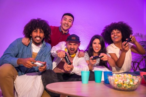 Adult party. Attractive young men sitting on the sofa playing video games with popcorn. Expressing joy while holding the joystick and looking at the monitor
