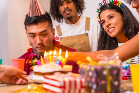 Multi-ethnic group of friends at a birthday party on the sofa at home with a cake and gifts