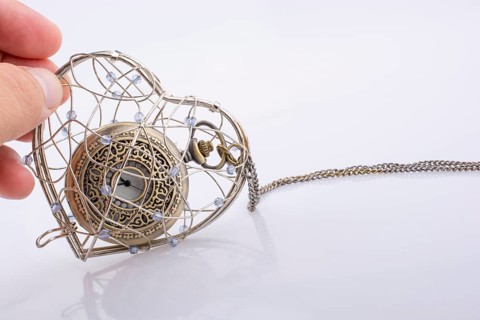 Pocket watch in a heart shaped metal wire cage in hand