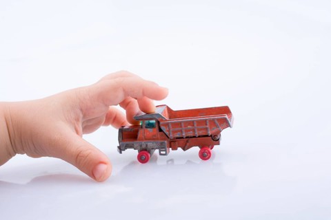 Baby hand is about to grab a red toy truck on white background