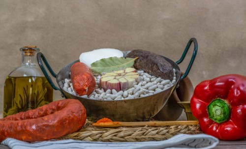 Raw white beans in metal casserole with all the ingredients for cooking them