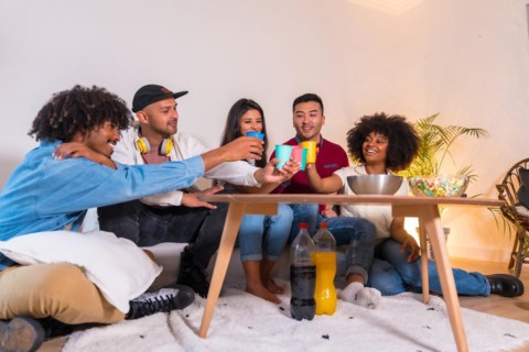 Group of friends eating popcorn and toasting with soft drinks. Laughing while watching a funny movie on TV at home