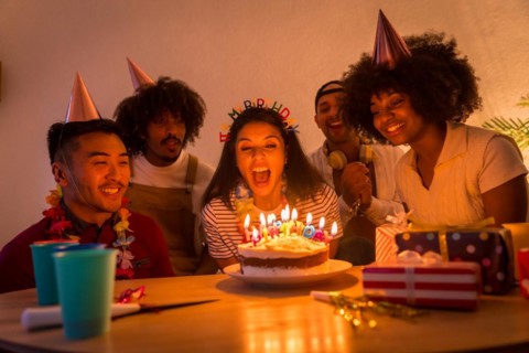 Multi-ethnic group of friends at a birthday party on the sofa at home with a cake and gifts