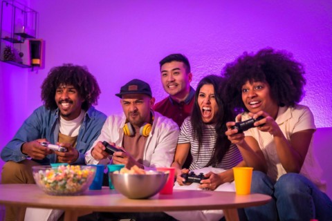 Adult party. Young people sitting on the sofa playing video games with popcorn. Joystick or controller in hand