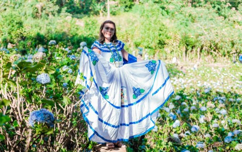 Smiling woman in national folk costume in a field surrounded by flowers. People in Nicaraguan national folk costume. Young Nicaraguan woman in traditional folk costume in a field of Milflores