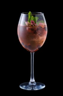Cold red sangria with dry rosebuds in a wine glass isolated on black background