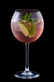 Cold sangria with lime and mint in a wine glass isolated on black background