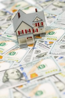 Small model house on layer of one hundred dollar bills