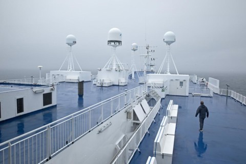 A man in drizzle and foggy weather on the deck of the ferry Norroena with marine electronics and the North Atlantic
