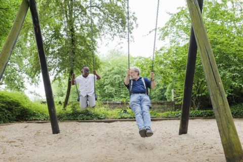 Temporary grandparents. Grandfather swinging with his charge in a playground.