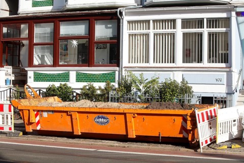 Orange skip for construction waste standing on the road in front of residential buildings