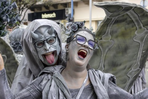 Young smiling woman with wings in grey and the devil masked at the carnival in the city of Rijeka