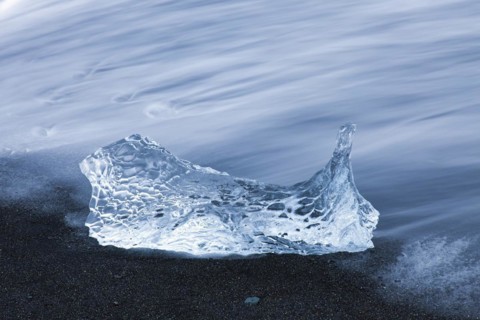 Melting block of ice washed on beach along the Atlantic Ocean coastline at Breidamerkursandur black sands in winter