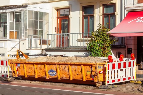 Orange skip for construction waste standing on the road in front of residential buildings