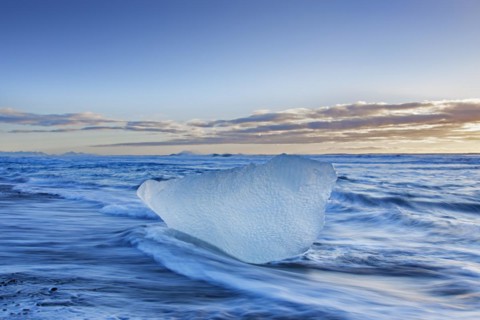 Melting block of ice washed on beach along the Atlantic Ocean coastline at Breidamerkursandur black sands in winter
