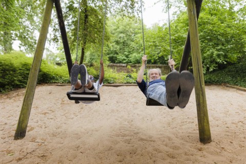 Temporary grandparents. Grandfather swinging with his charge in a playground.