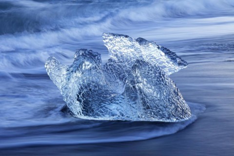 Melting block of ice washed on beach along the Atlantic Ocean coastline at Breidamerkursandur black sands in winter
