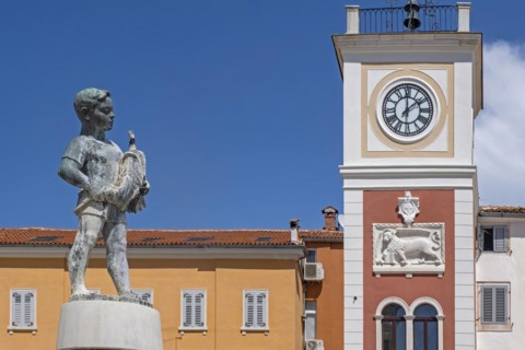 Boy with Fish fountain and 17th century red clock tower in the city Rovinj