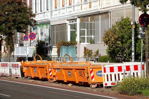 Orange skip for construction waste standing on the road in front of residential buildings