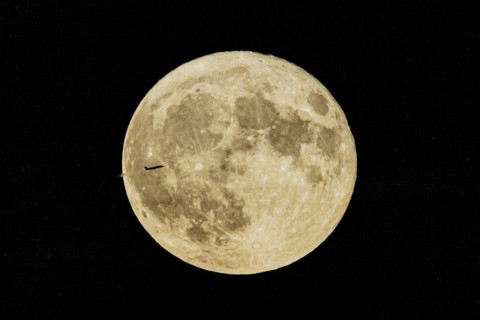 A plane looms in front of the so-called strawberry moon looms as it rises in Berlin