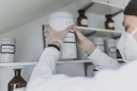 An employee in a pharmacy uses a stand-up container with base cream DAC in the prescription