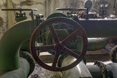 Cobwebs on a rusted shut-off wheel on a water pipe of a former paper factory